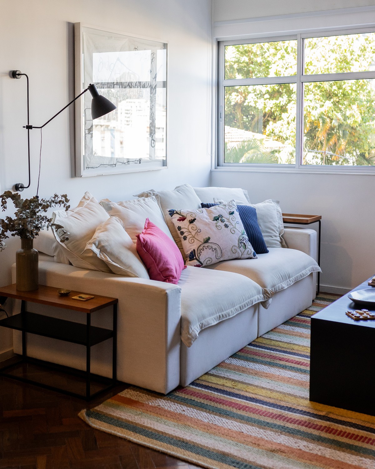 Sala com sofá branco, almofadas coloridas e luminária de parede articulada