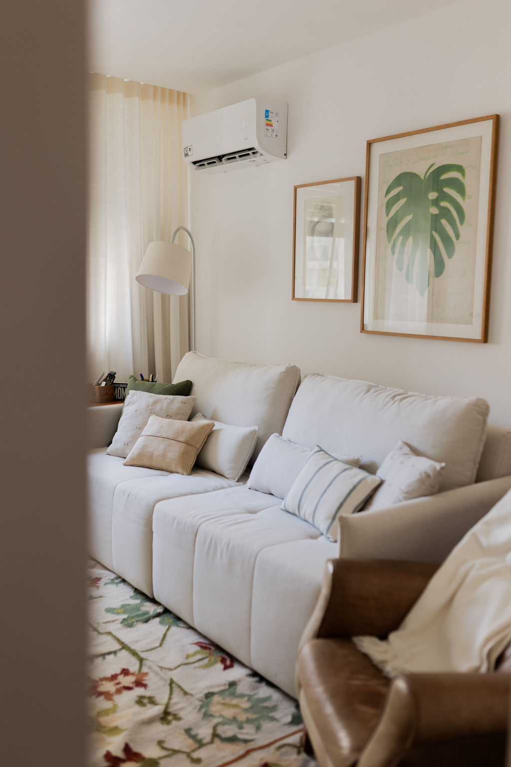 Sala clara com sofá branco, poltrona de couro e tapete floral