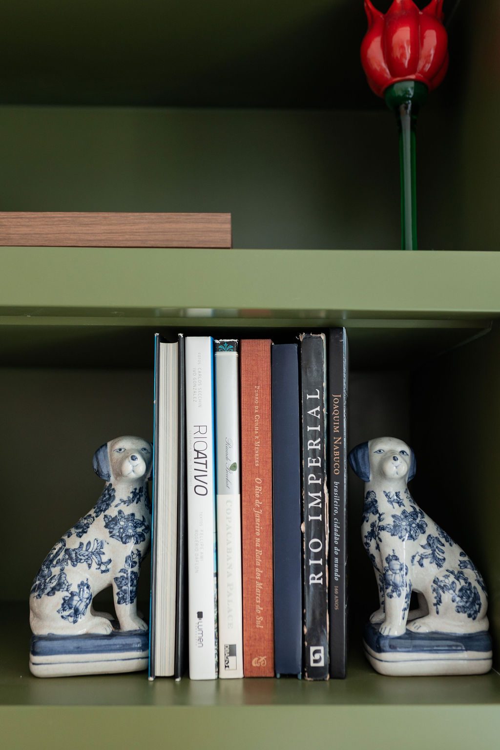 Detalhe da estante verde com livros e cães de porcelana
