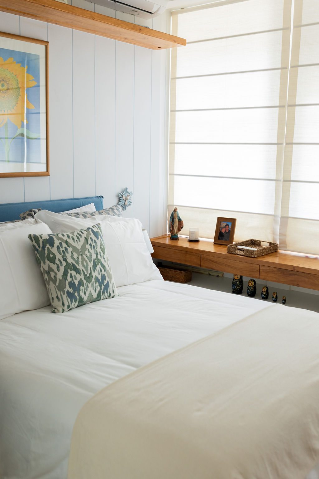 Cama de casal com almofadas estampadas junto à janela