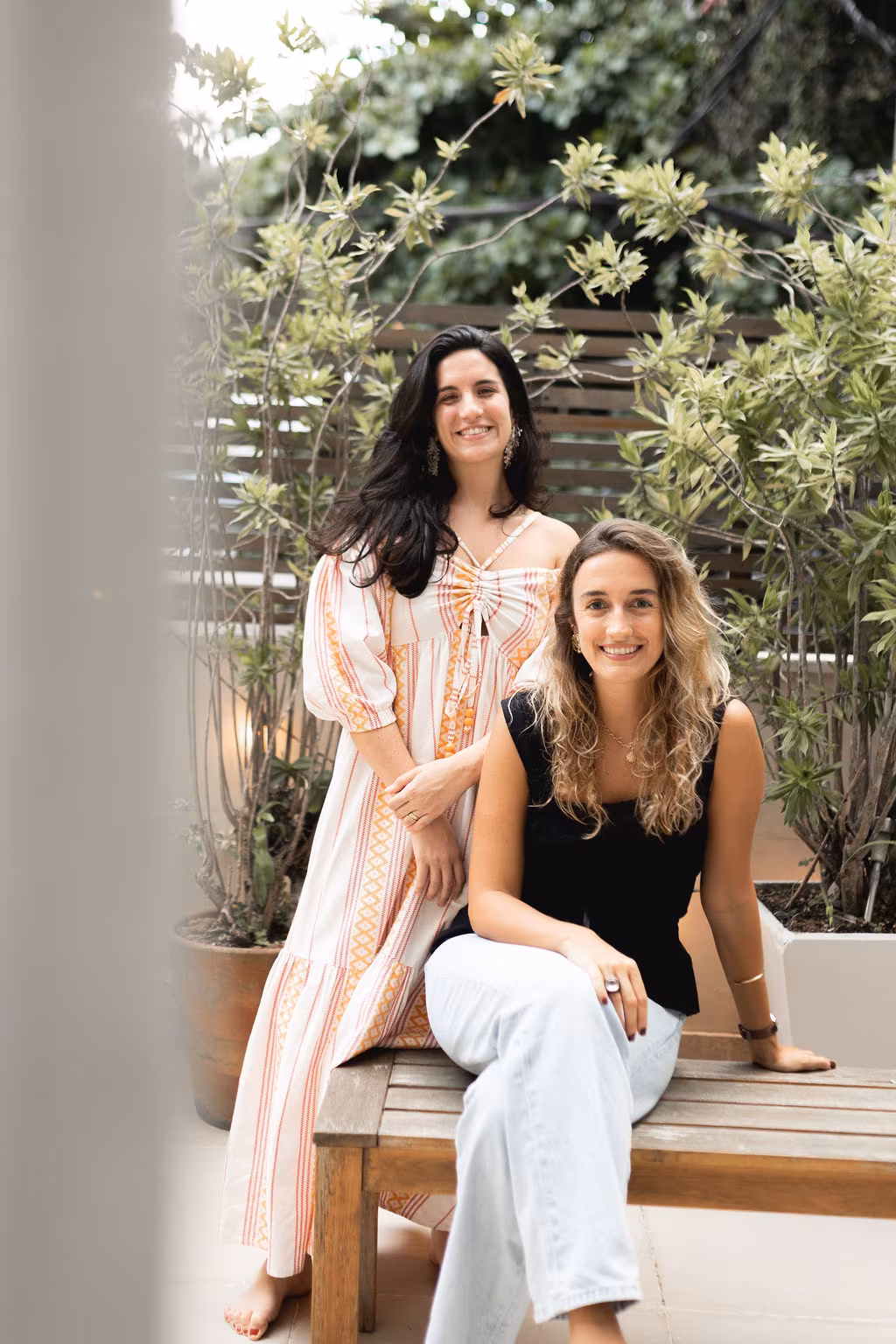 Marina e Catharina, sócias da Teçá, em um jardim com plantas ao fundo