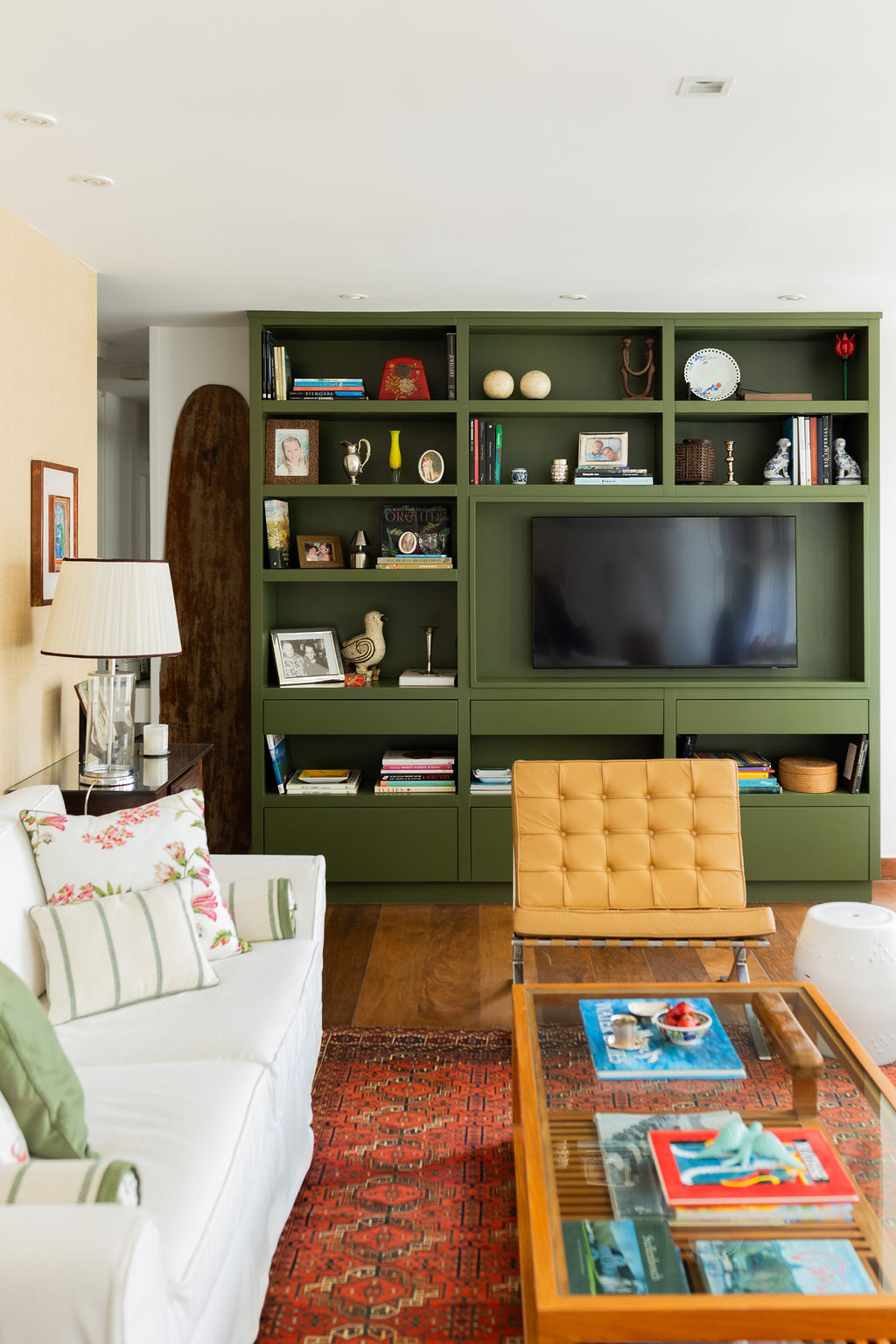 Sala de estar com estante verde, poltrona de couro e tapete vermelho