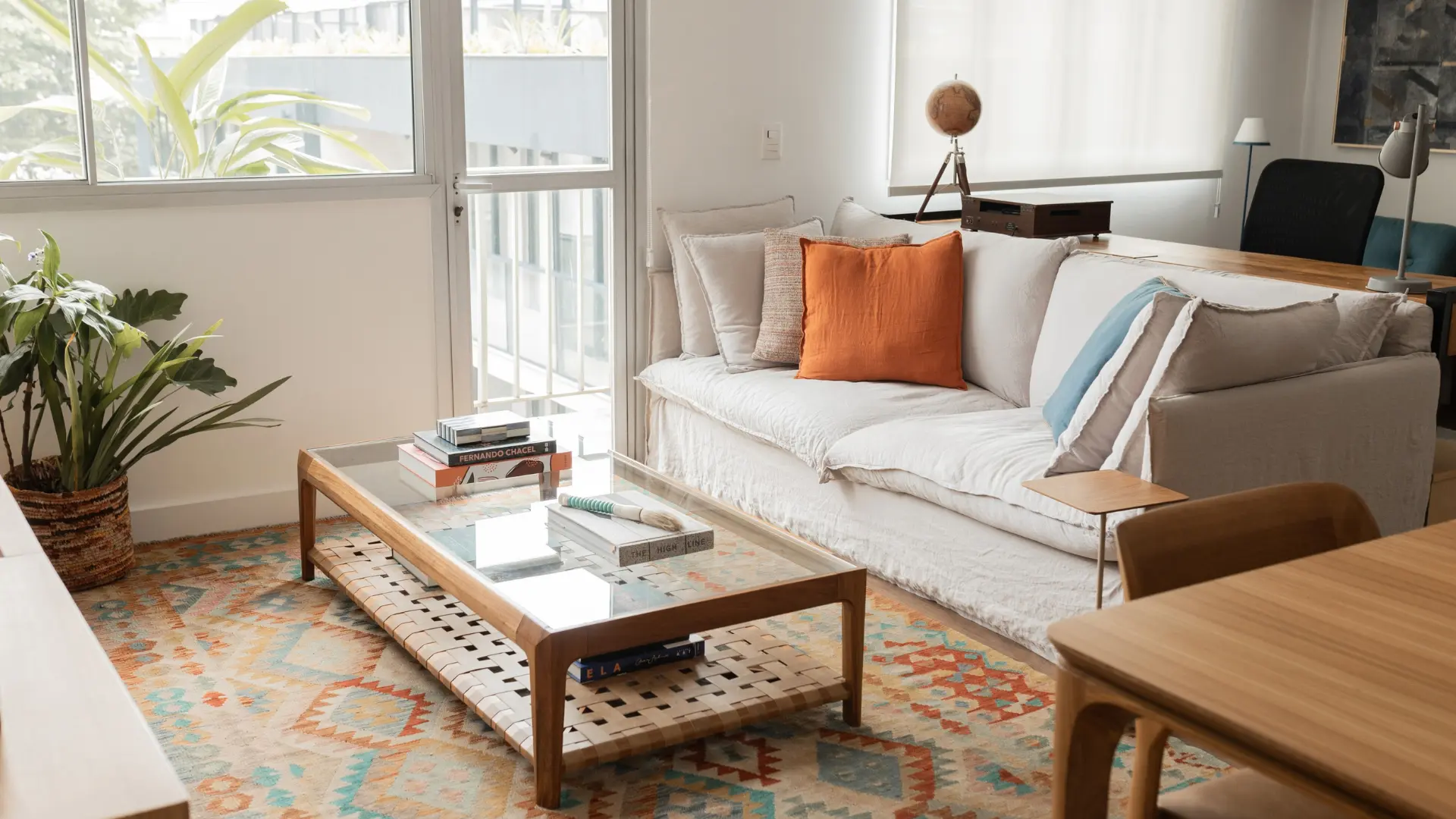 Sala de estar pronta, com sofá claro, mesa de centro de madeira e vidro e tapete colorido