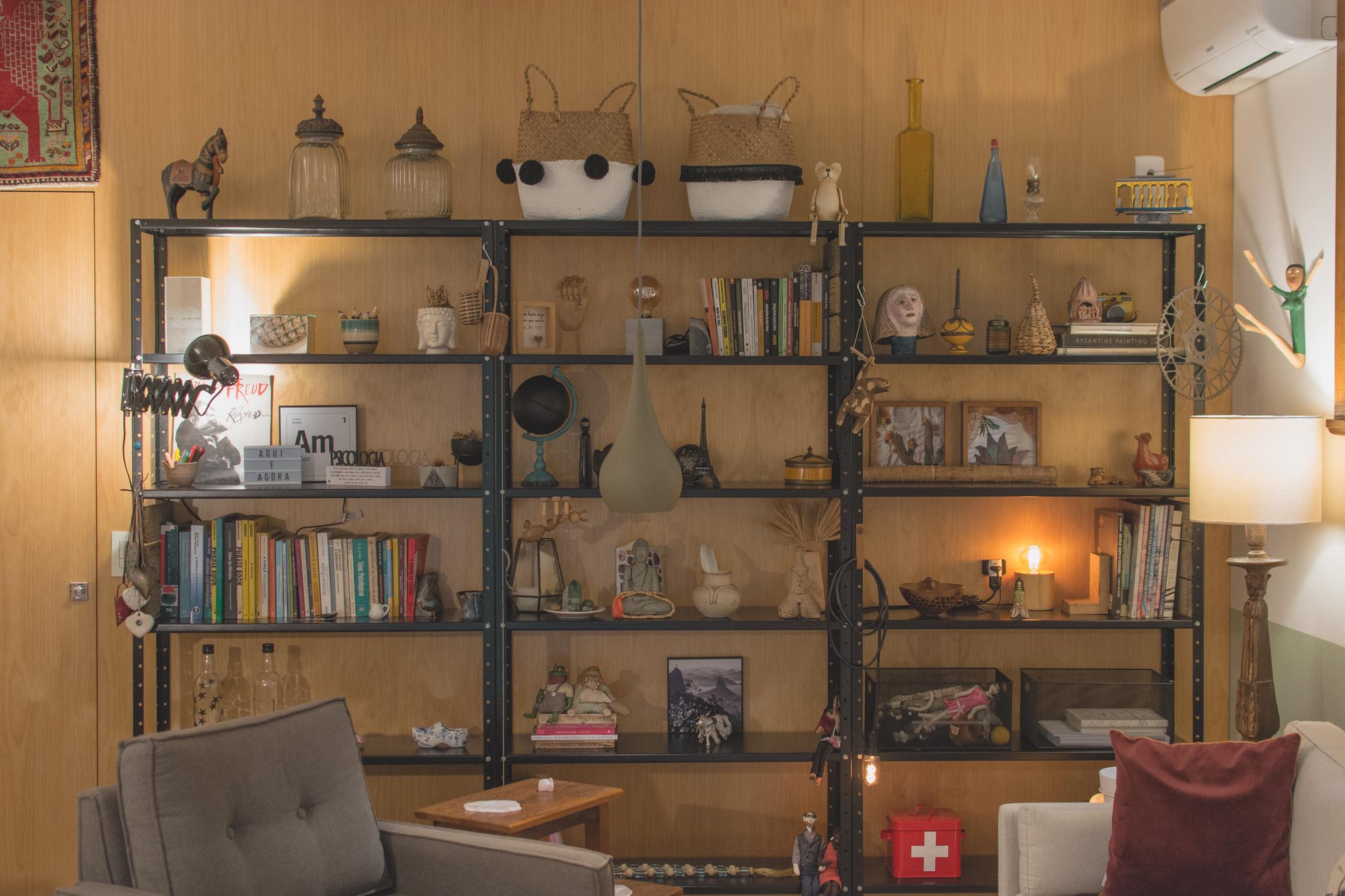 Estante de serralheria com livros e objetos, sofá e poltrona