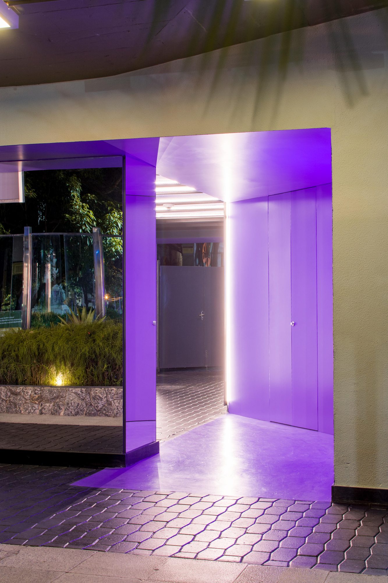Passagem iluminada em lilás com jardim ao lado